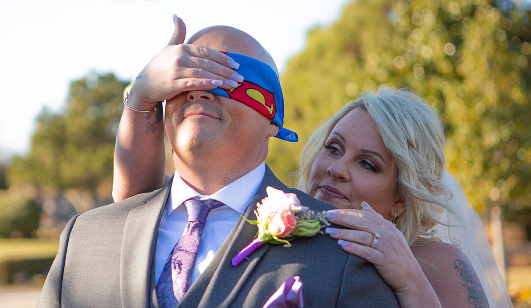 Groom with superman blindfold, bride behind him