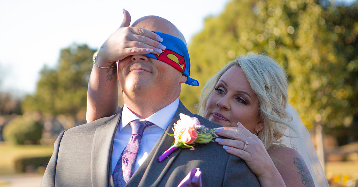 Groom with superman blindfold, bride behind him