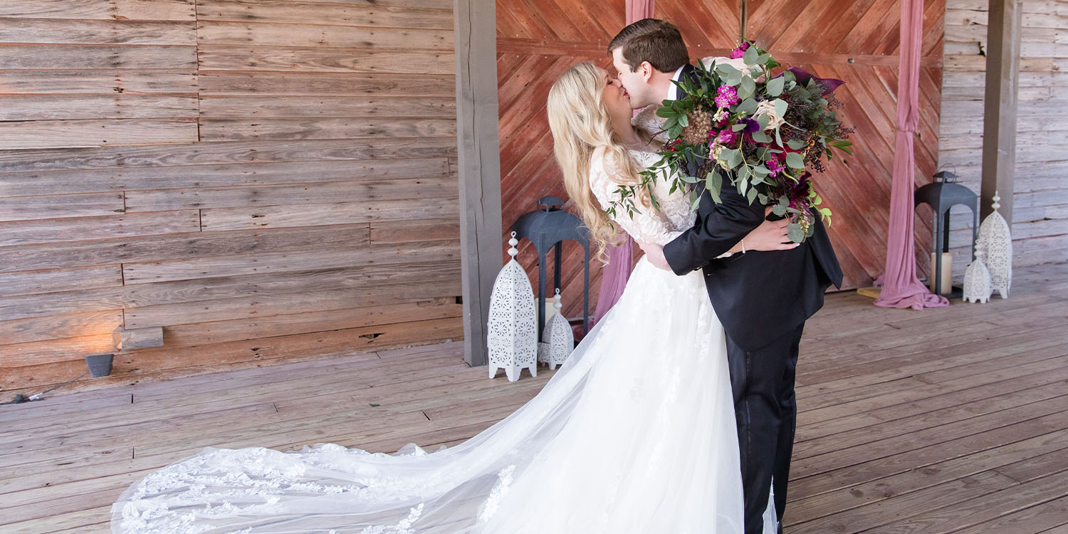 Newly married coupld embracing and kissing infront of wooden barn
